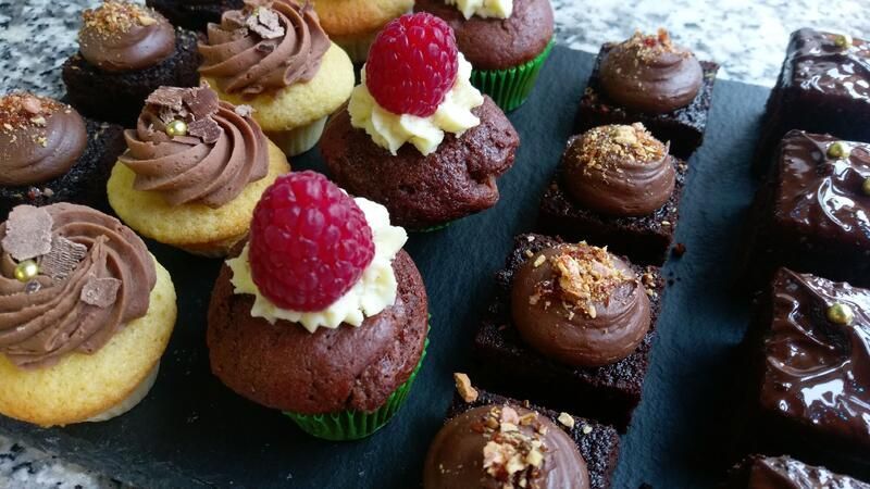 Ein Tablett mit Cupcakes und Brownies, belegt mit Himbeeren.