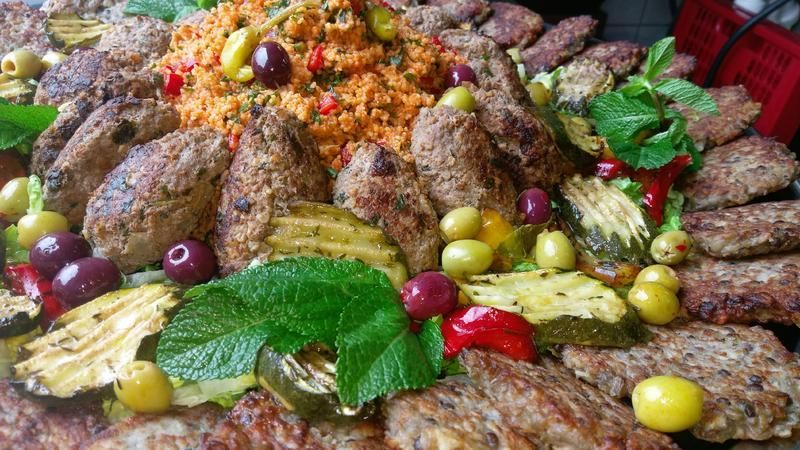 Ein Teller mit Fleischbällchen, Oliven, Reis und Gemüse auf einem Tisch.