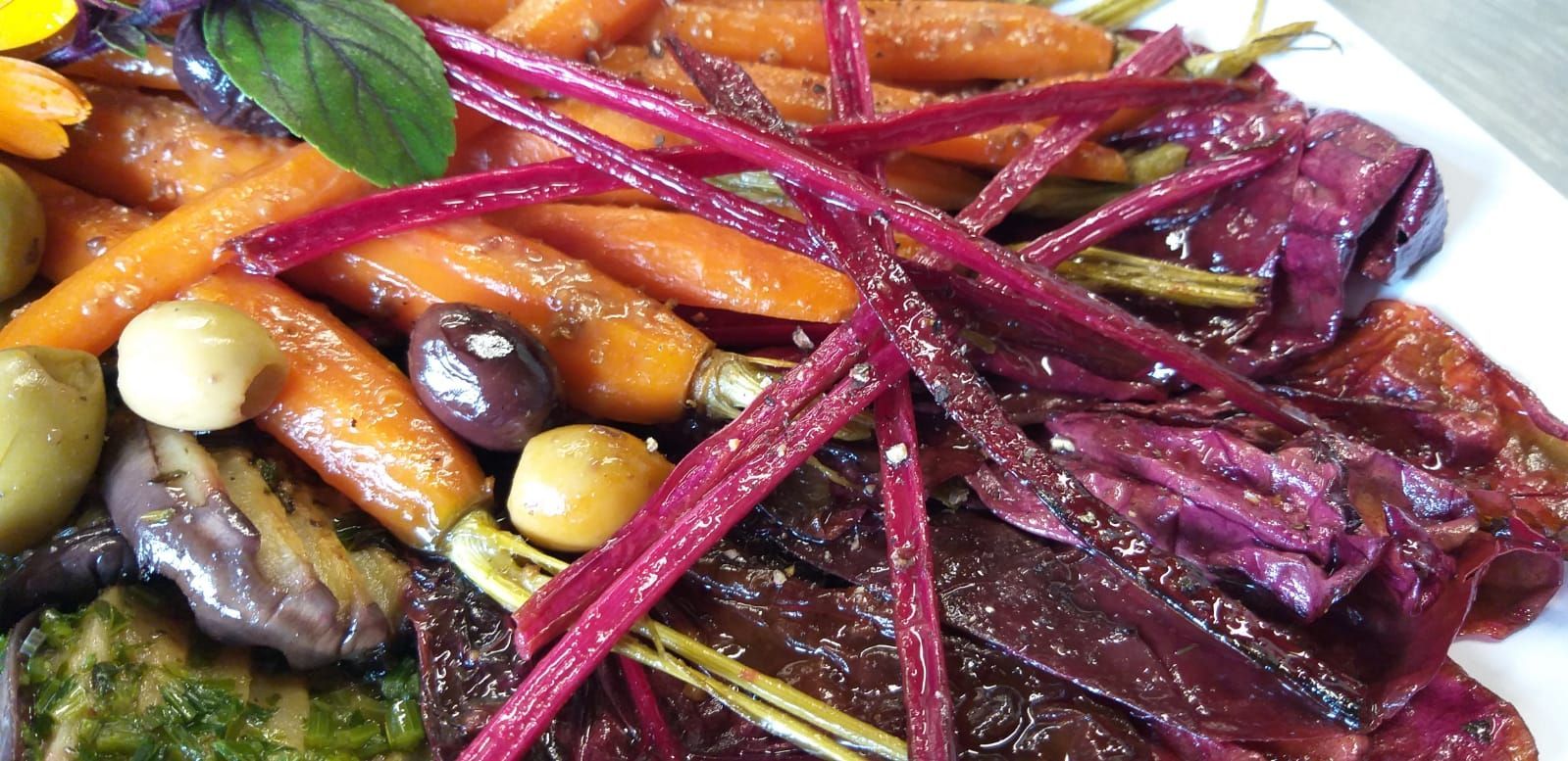 Ein weißer Teller, belegt mit Karotten, Rüben, Oliven und anderem Gemüse.