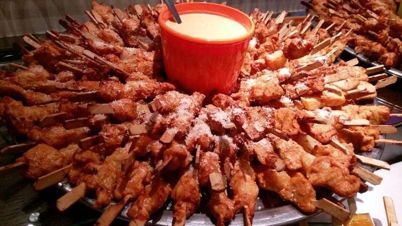 Ein Tablett mit Hühnchenspießen und einer Schüssel Dip-Sauce in der Mitte.
