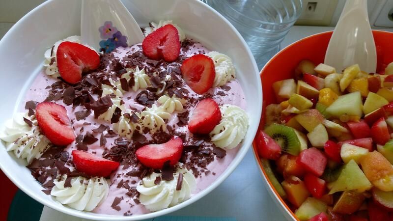 Eine Schüssel mit Erdbeeren und Schlagsahne neben einer Schüssel Obstsalat