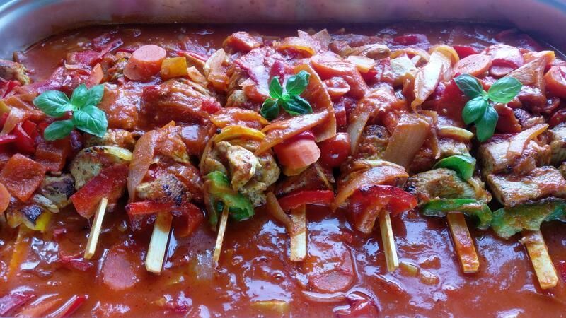 Ein Tablett mit Fleisch- und Gemüsespießen in einer Soße.