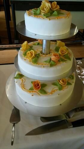 Auf einem Tisch steht eine dreistöckige Hochzeitstorte mit gelben Rosen obendrauf.