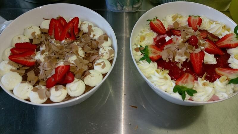 Zwei Schüsseln Dessert mit Schlagsahne und Erdbeeren auf einem Tisch.