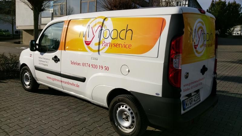 Ein weißer Lieferwagen mit gelber und orangefarbener Beklebung steht auf einem Parkplatz.