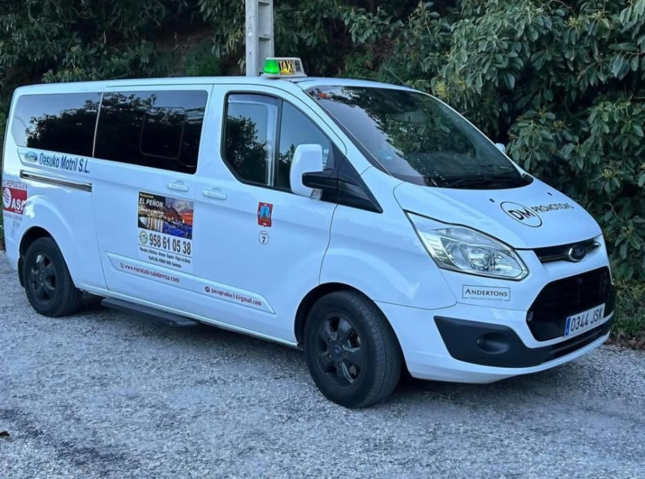 Furgoneta de reparto blanca aparcada en un camino de grava junto a unos árboles, con pegatinas publicitarias en el lateral.