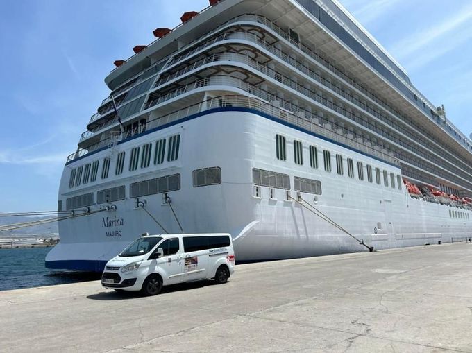 Un gran crucero blanco atracado en el puerto con una furgoneta blanca delante.