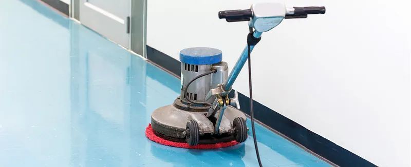 Una máquina está limpiando un piso azul en un pasillo.