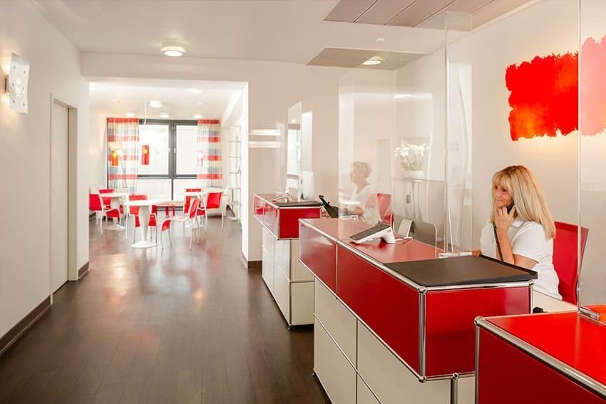 Eine Frau sitzt an einem roten Schreibtisch in einem Flur und telefoniert mit einem Mobiltelefon