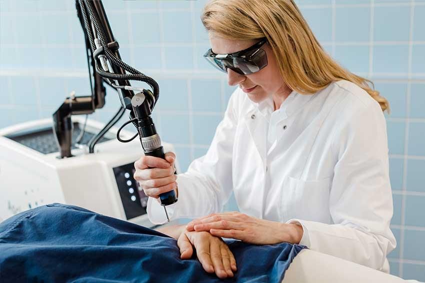 Eine Frau verwendet einen Laser an der Hand eines Patienten.