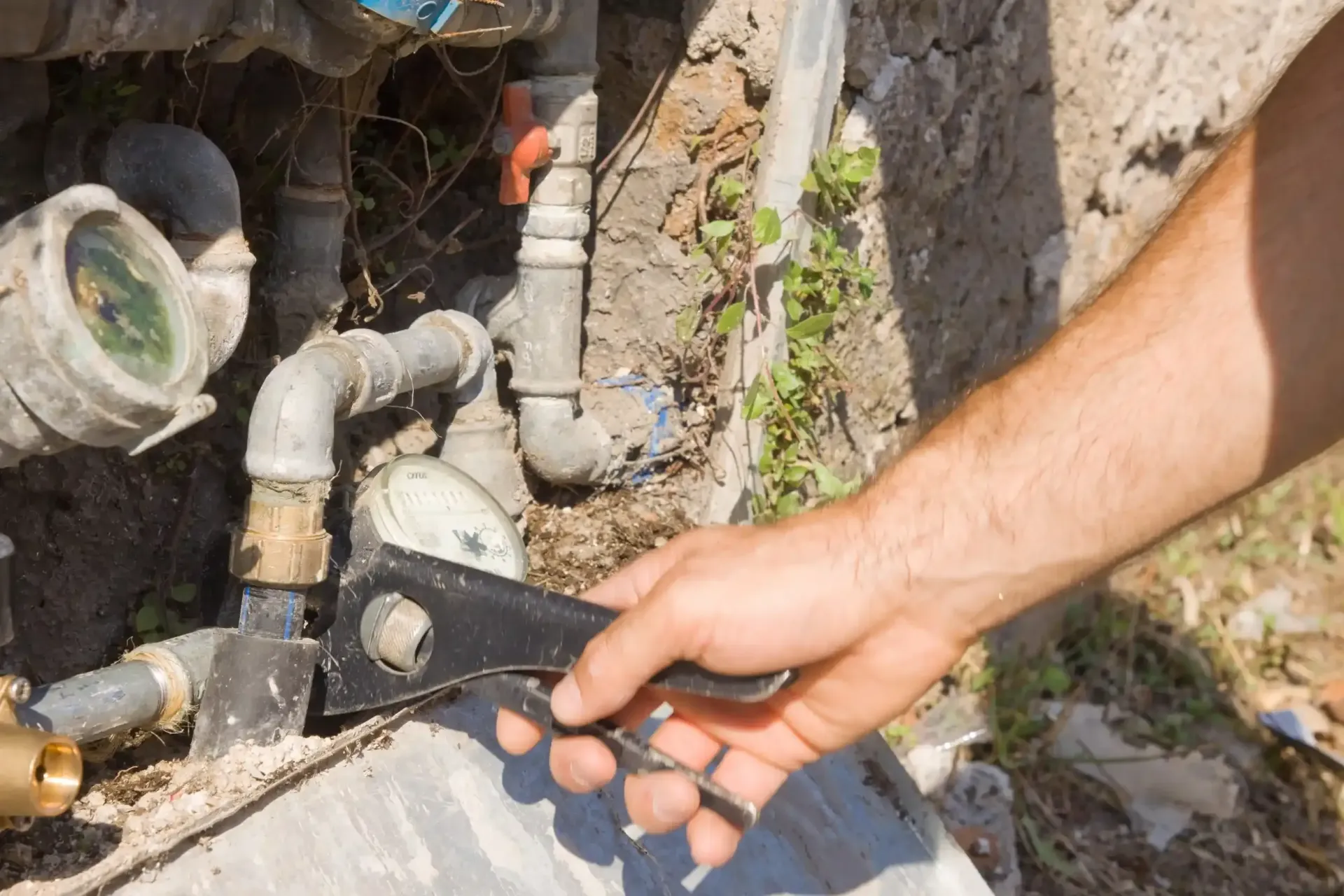 Cerrando a mano una llave inglesa negra en tuberías de fontanería exteriores junto a una pared.