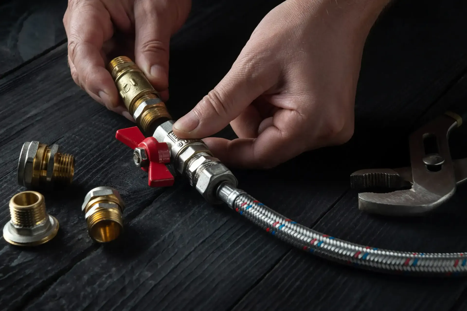 Manos ensamblando un racor de manguera de latón con una llave inglesa sobre una superficie de trabajo oscura.