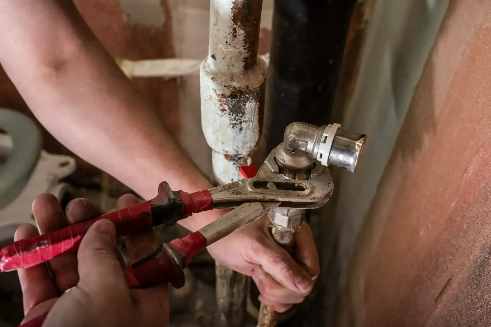 Un fontanero utiliza una llave inglesa roja para apretar una válvula de tubería contra la pared.