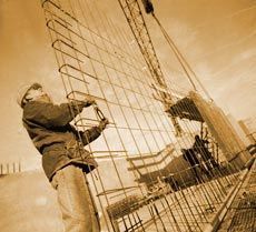 Un hombre está trabajando en una valla con una grúa al fondo.