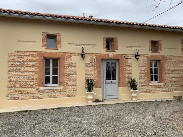 Devanture de maison recouverte d'un enduit beige et encadrement des fenêtres en briques foraines