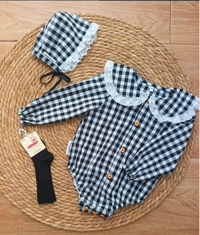 Un bebé lleva un traje a cuadros blanco y negro con gorro y calcetines.