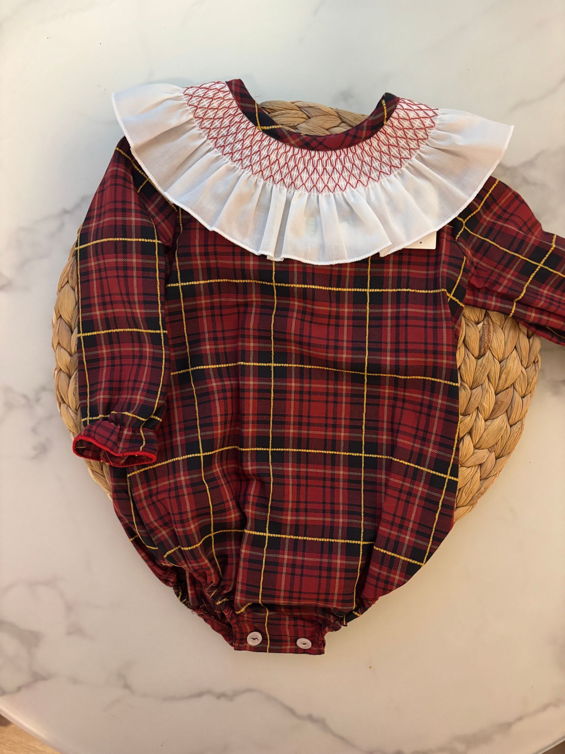 Un bebé lleva un mono de cuadros rojos con cuello blanco.