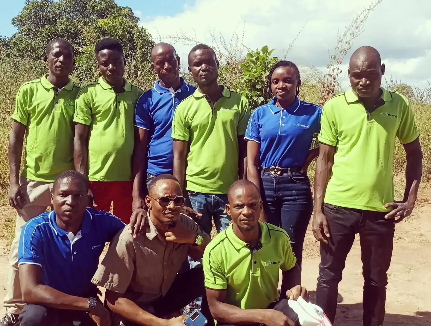 Grupo de pessoas posando ao ar livre, a maioria vestindo camisas verdes e azuis.