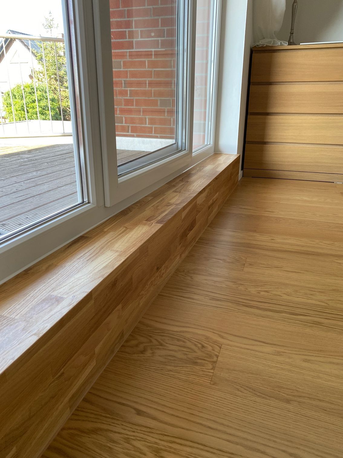 Ein Holzboden neben einem Fenster mit einer Ziegelwand im Hintergrund.
