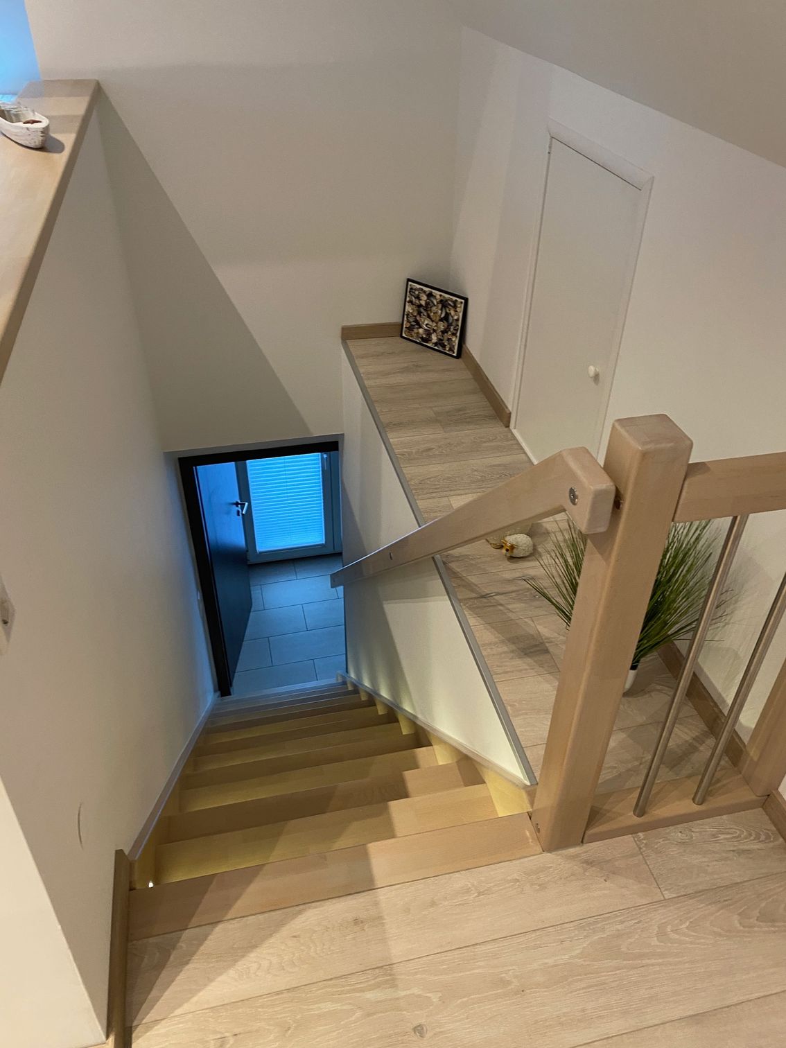 Eine Holztreppe mit Glasgeländer führt in den zweiten Stock eines Hauses.