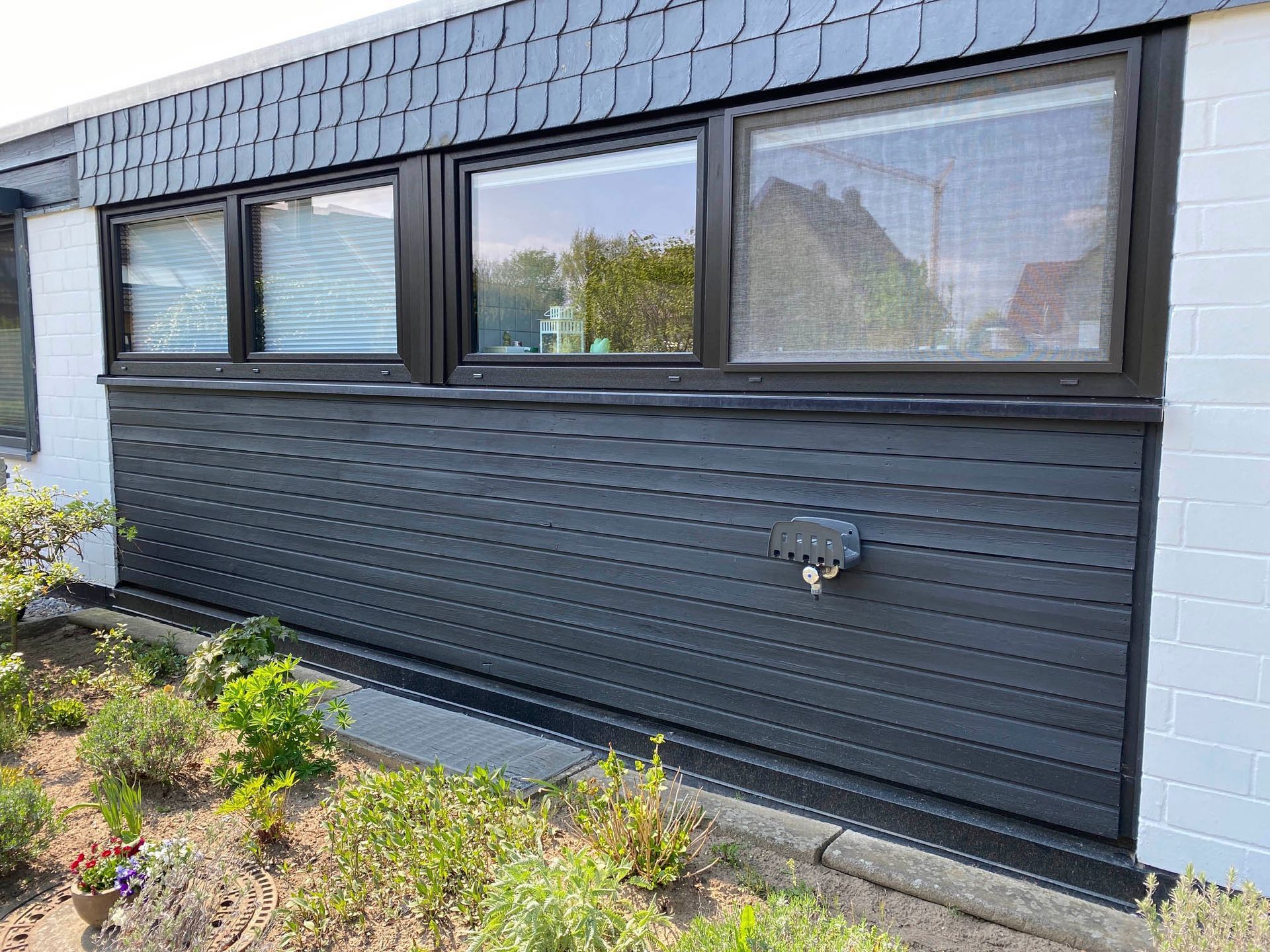 Ein Haus mit schwarzer Außenverkleidung und vielen Fenstern.