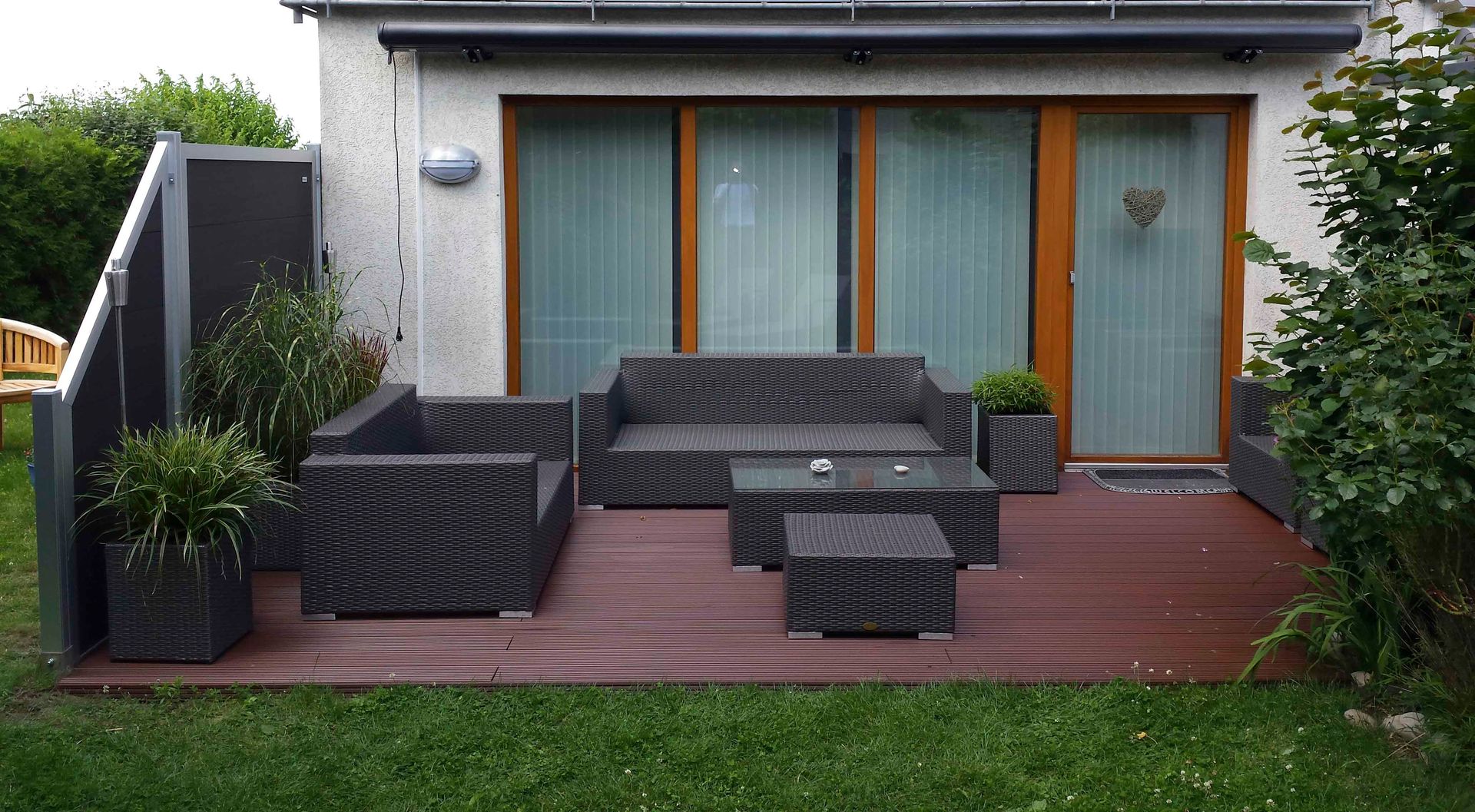 Eine Terrasse mit Sofa, Stühlen und Tisch vor einem Haus.