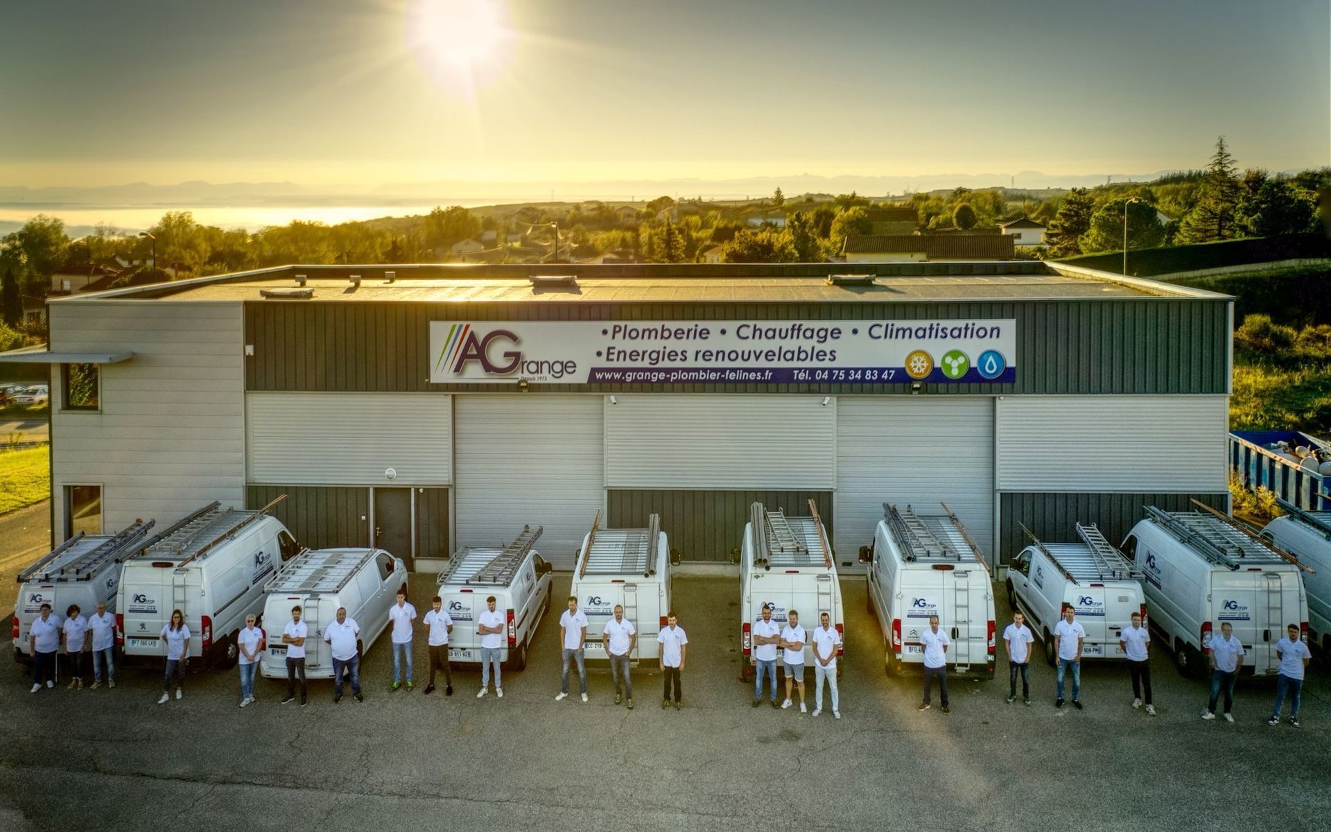 Equipe posant devant un bâtiment avec des camionnettes de service, sous un ciel ensoleillé.
