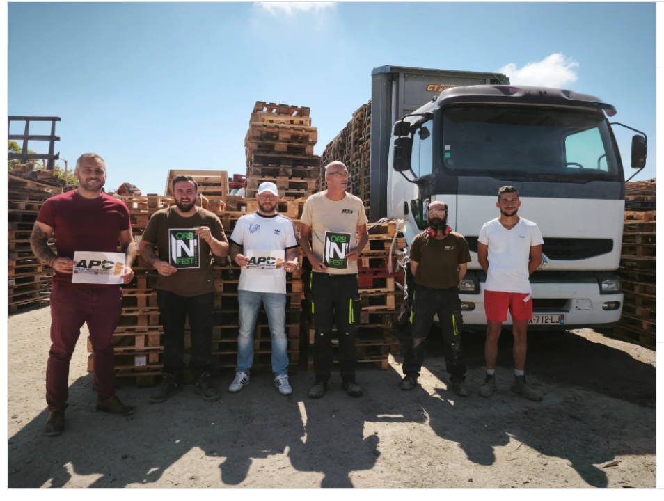 Six hommes se tiennent debout près de palettes empilées à côté d'un camion blanc.