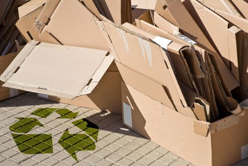 Des cartons et des déchets d'emballage s'entassent sur un trottoir à côté d'un symbole de recyclage vert peint sur la chaussée.