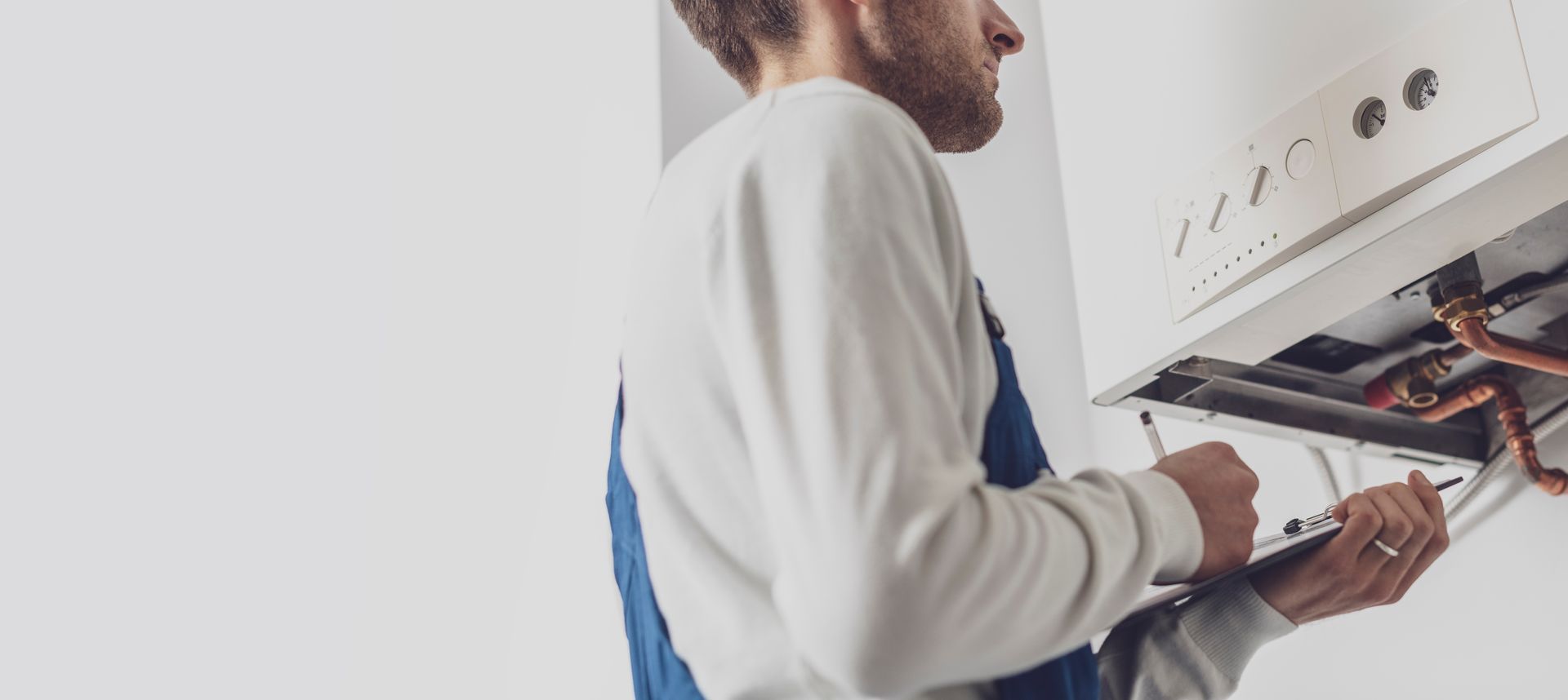 Un technicien inspecte une chaudière et prend des notes sur un presse-papiers dans une salle blanche.