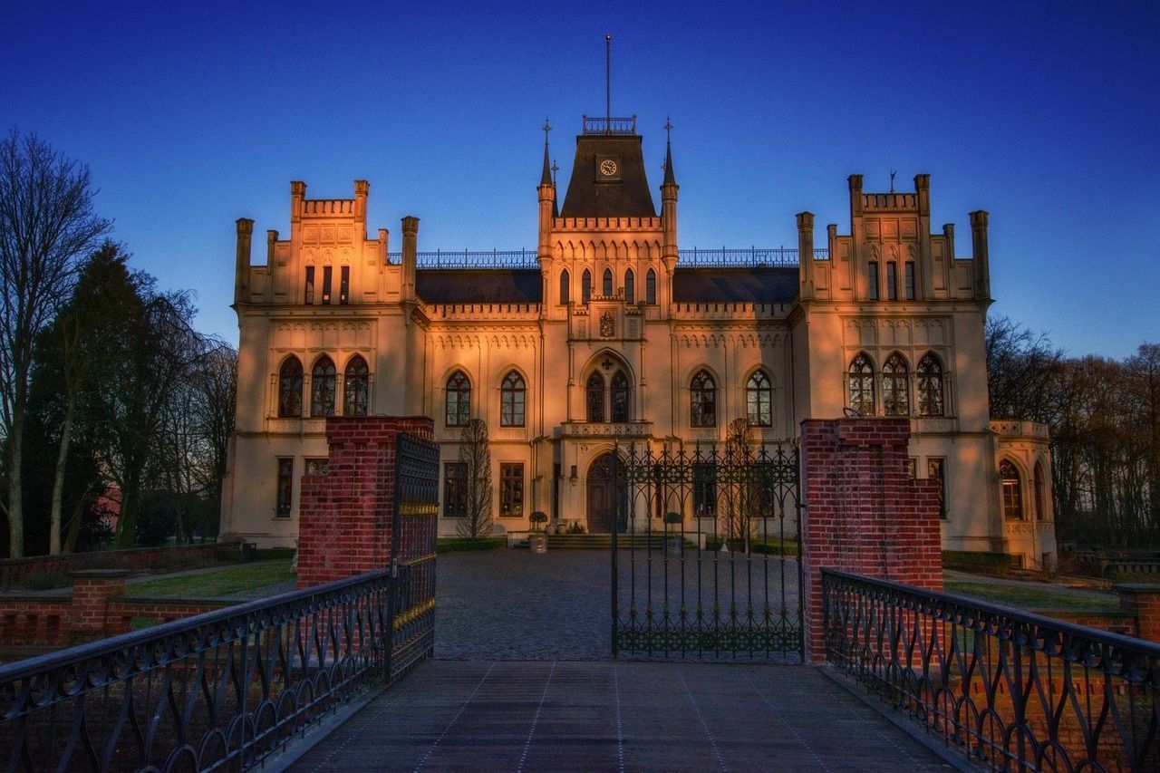 Ein prunkvolles Schloss mit Bogenfenstern, Türmchen und einem Eingangstor, das von goldenem Sonnenlicht vor blauem Himmel erhellt wird.