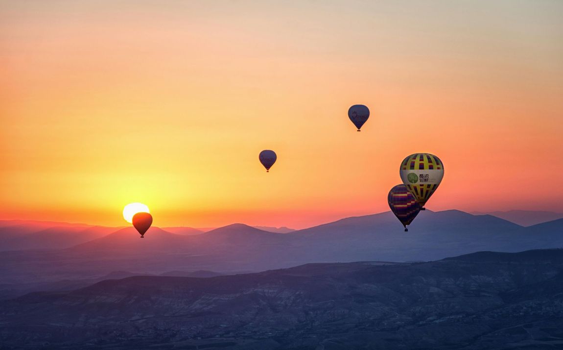 Eine Gruppe Heißluftballons fliegt bei Sonnenuntergang am Himmel.