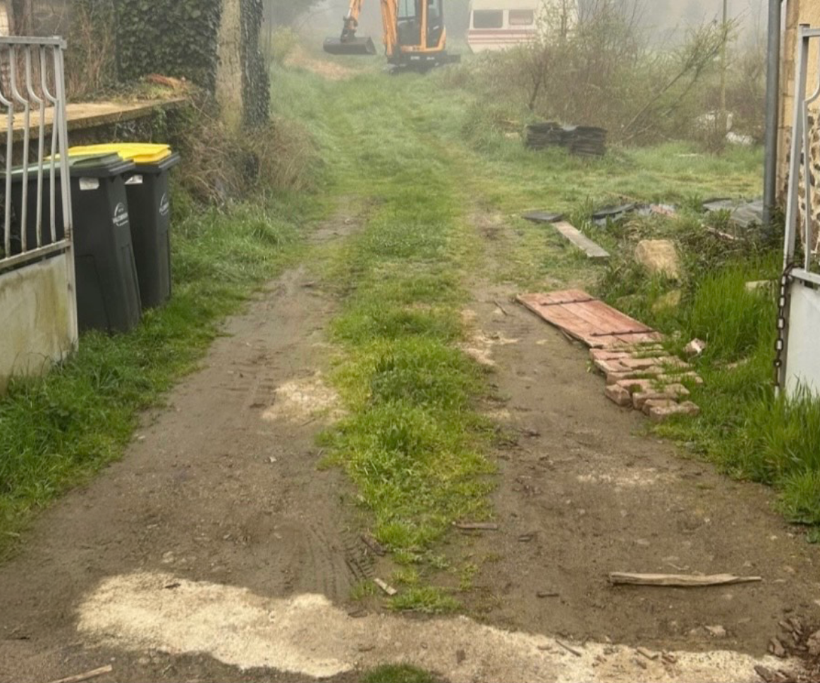 Un chemin de terre menant à une maison avec un bulldozer en arrière-plan.