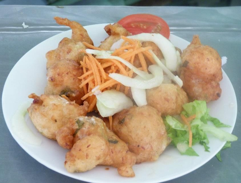 Assiette de nourriture frite, comprenant des boules rondes, avec des carottes râpées, des oignons, des tomates et de la laitue.