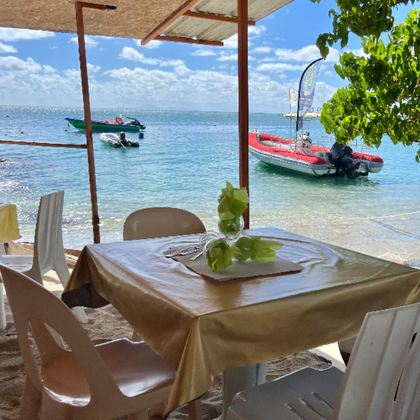 Une table dressée pour dîner dans un restaurant en bord de mer, avec l'océan et les bateaux en arrière-plan.