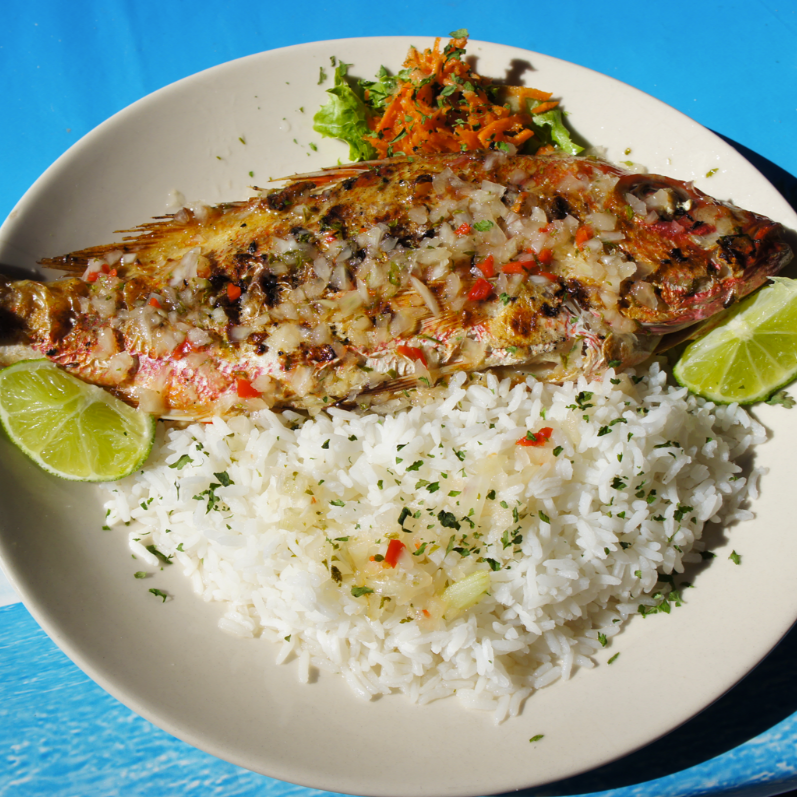Poisson entier grillé avec riz, quartiers de citron vert et légumes d'accompagnement dans une assiette.