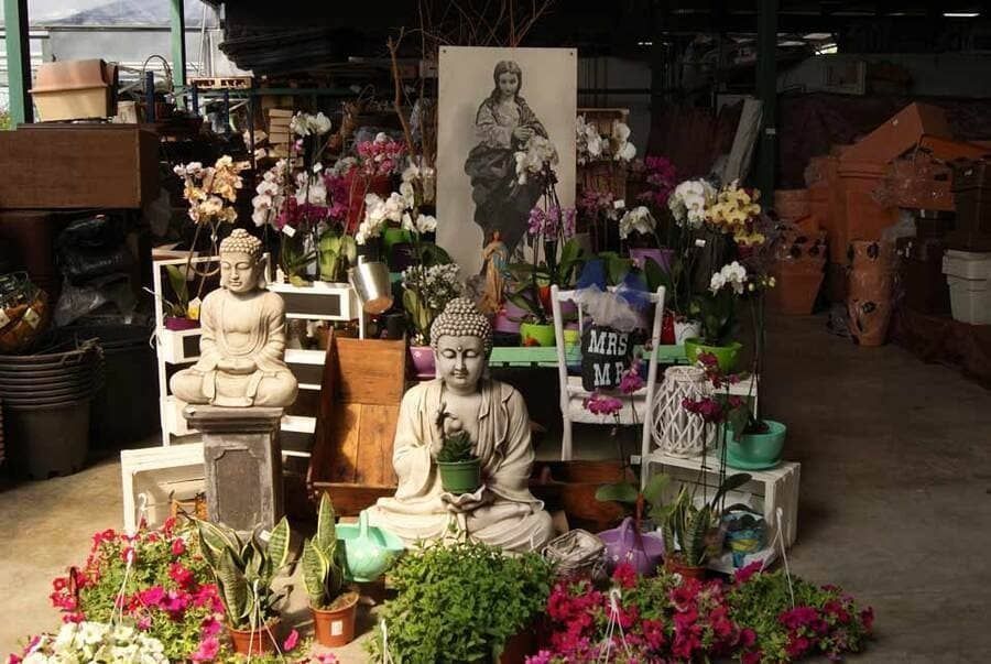 Estatuas de Buda y arreglos florales en un puesto de mercado, con un gran retrato detrás