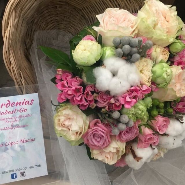 Ramo floral en rosa pastel y blanco con algodón y rosas en una cesta de mimbre, junto a una tarjeta de Gardenias Floral Co