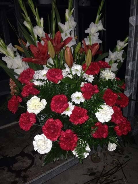 Arreglo floral rojo y blanco con gladiolos y claveles en un jarrón al aire libre por la noche