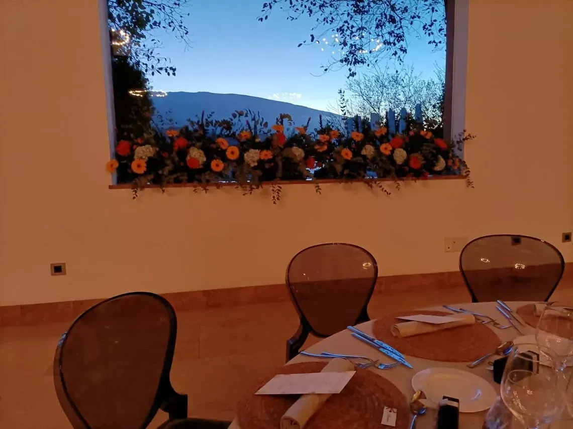 Mesa de comedor junto a una ventana decorada con flores, con colinas al otro lado.