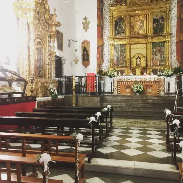 Altar de iglesia ornamentado con decoraciones doradas, bancos y suelo de baldosas blancas y negras