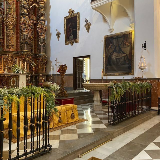 Altar de iglesia ornamentado con decoraciones doradas, cuadros enmarcados y plantas en macetas en un santuario con suelo de baldosas.