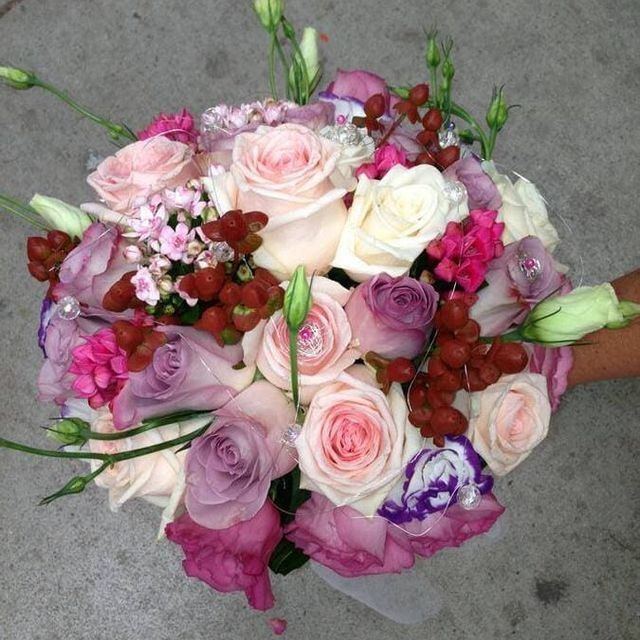 Ramo de rosas rosas y blancas variadas, con flores moradas y bayas rojas, sobre un pavimento gris