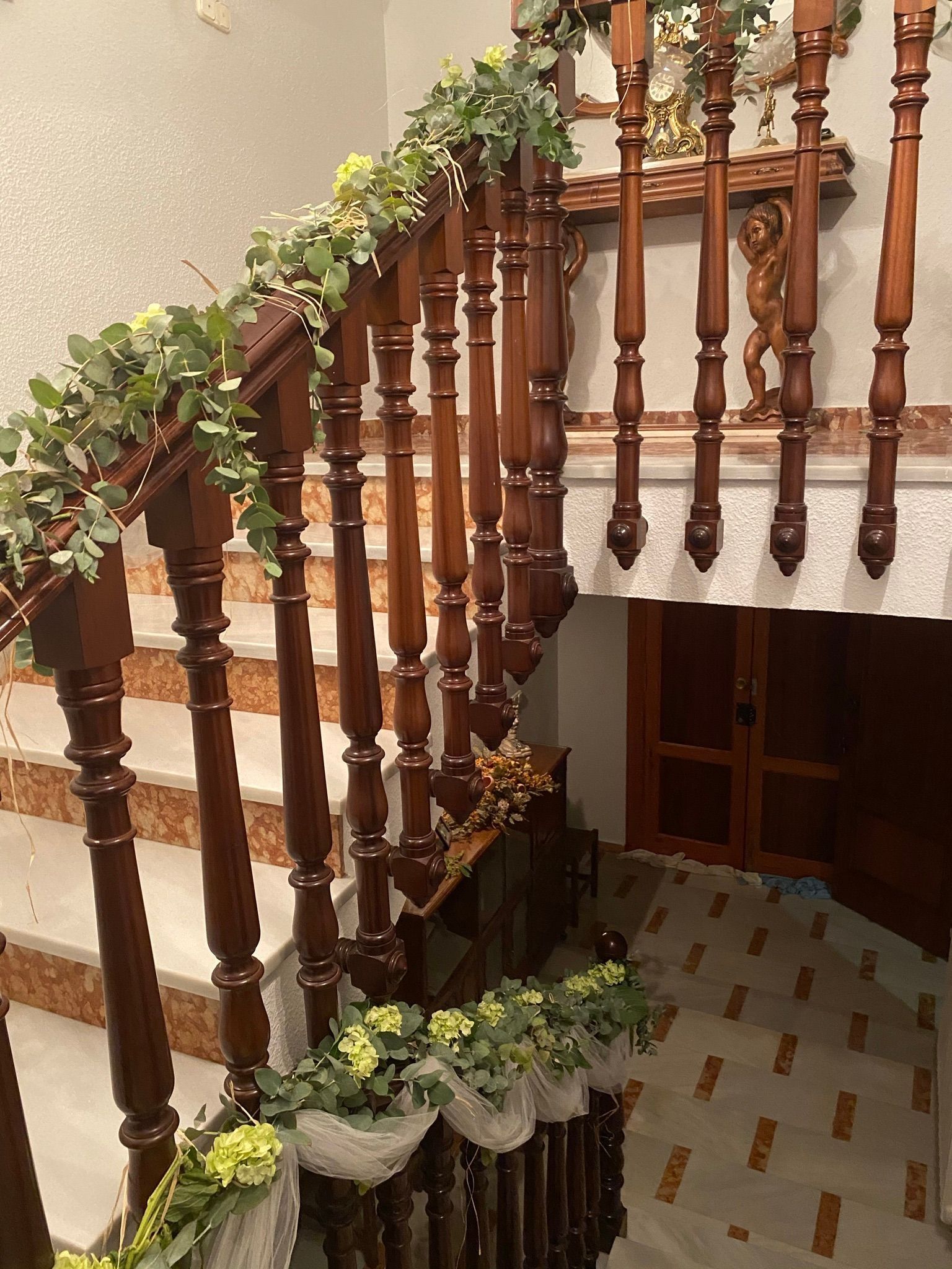 Escalera de madera decorativa con balaustres tallados y guirnalda verde a lo largo de la barandilla
