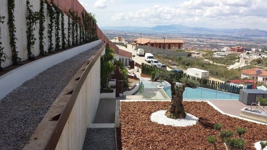 Jardín en una ladera aterrazada, con un sendero sinuoso, plantas en macetas y vistas lejanas del valle bajo un cielo luminoso