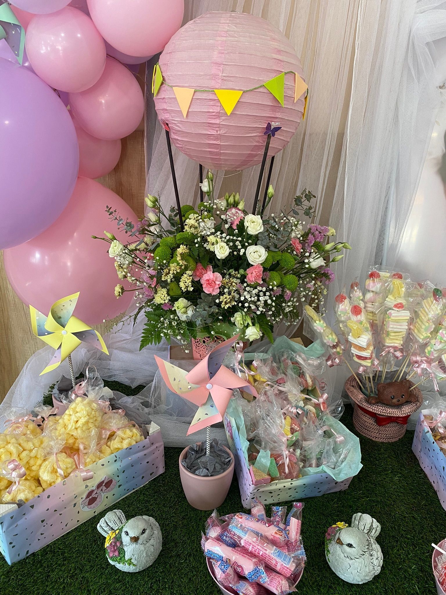 Decoración de cumpleaños con globos y flores en tonos pastel, cestas de regalo y regalos envueltos