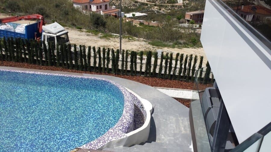 Piscina curva con agua de mosaico azul junto a una casa moderna y vistas a la ladera del monte