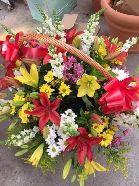 Colorido ramo de lirios, margaritas y flores rosas con una cinta roja en una cesta de mimbre