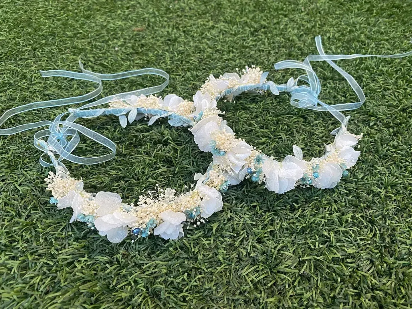 Guirnalda de flores blancas con cintas celestes sobre césped verde