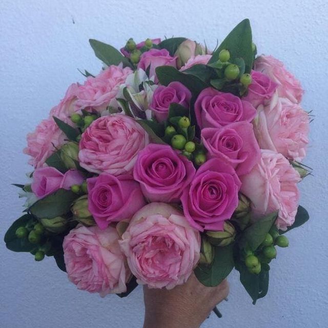 Ramo de mano de rosas rosas y bayas verdes con hojas verde oscuro